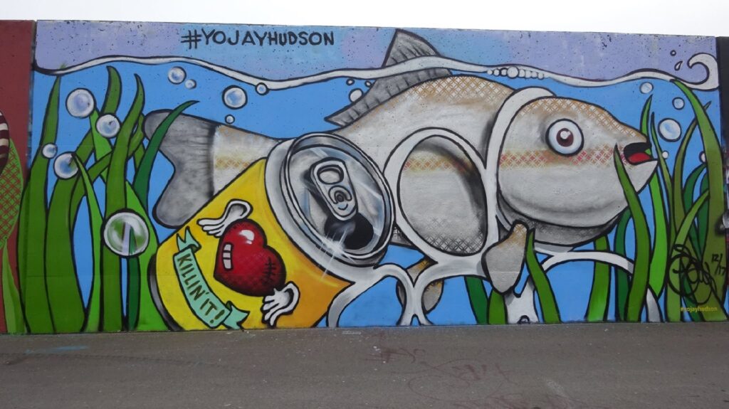 Mural of a fish under water caught in a plastic six pack plastic ring with one beer can attached